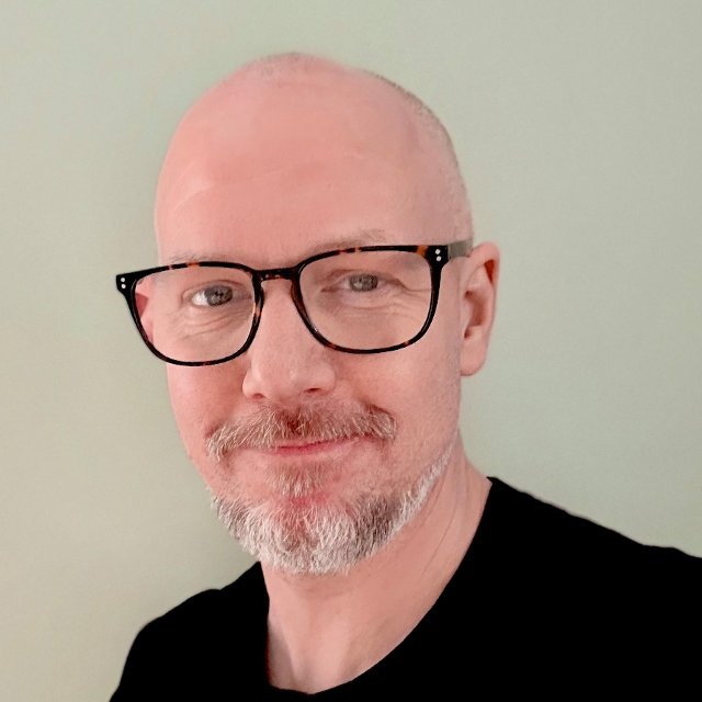 Mann med briller, ser smilende inn i kameraet.