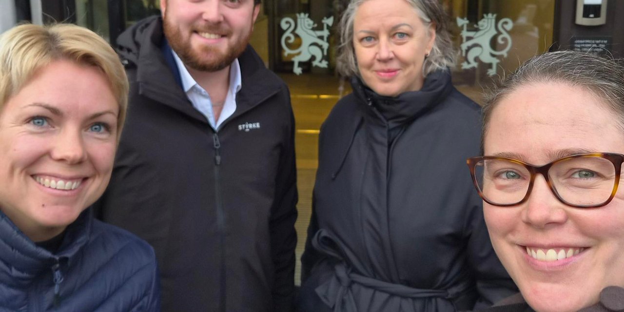 Personer står foran inngangen til Stortinget og smiler.