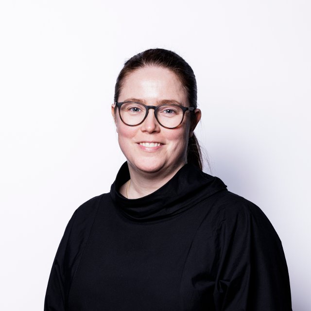 Kjersti Barsok, kvinne med briller som smiler inn i kamera med hvit bakgrunn.