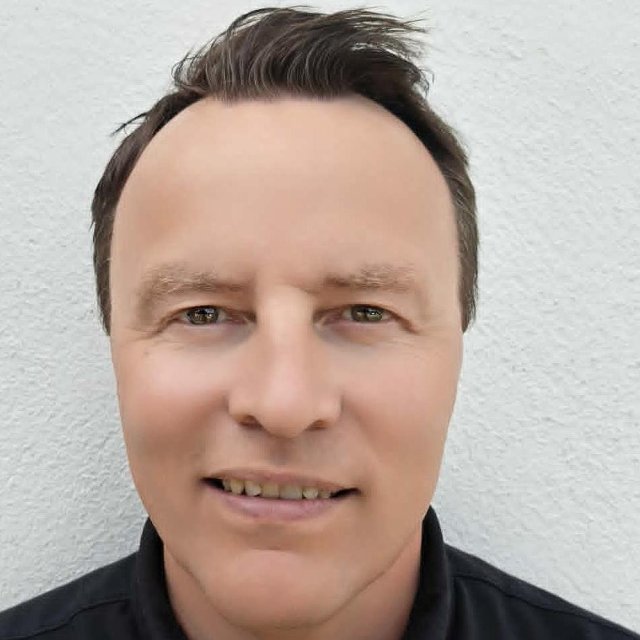 Mann ser smilende inn i kamera foran en hvit vegg.