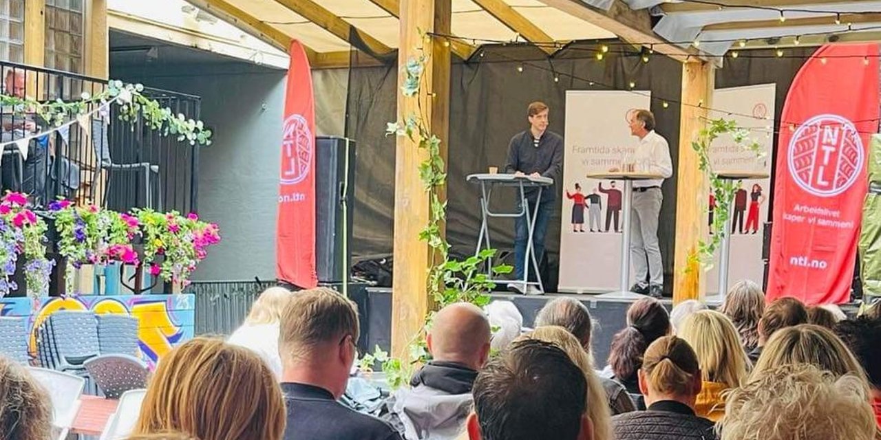 Publikum sitter foran en scene med NTL-roll-up under et arrangement på Arendalsuka.
