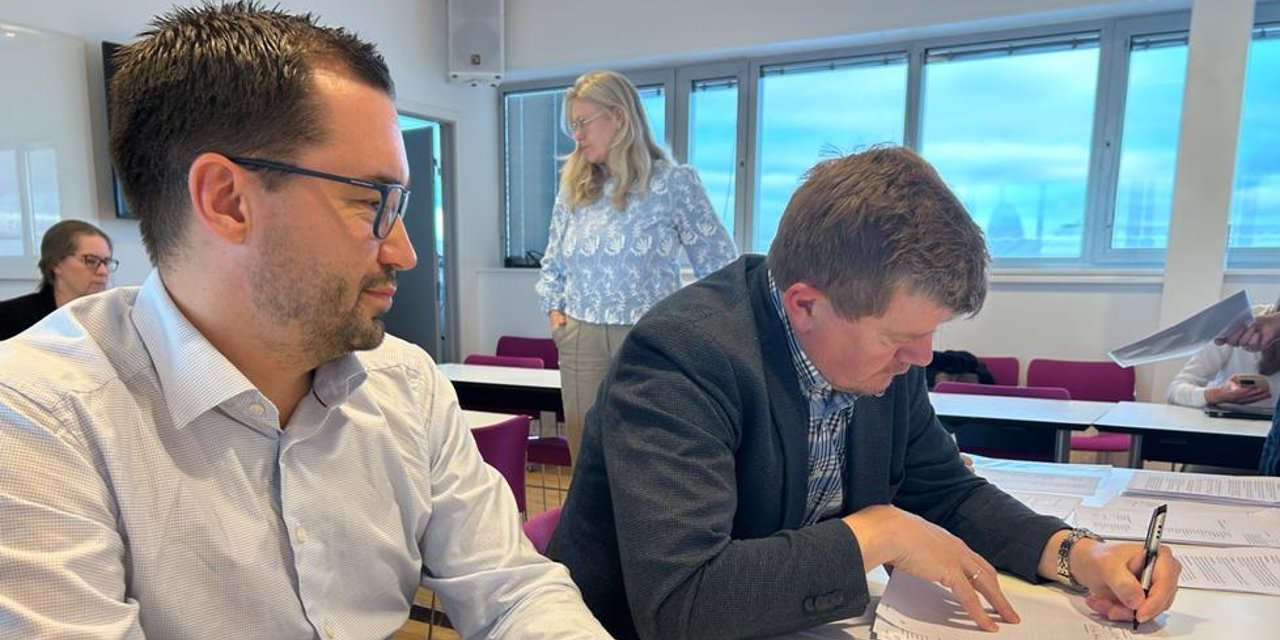 To menn sitter ved et bord og signerer dokumenter.
