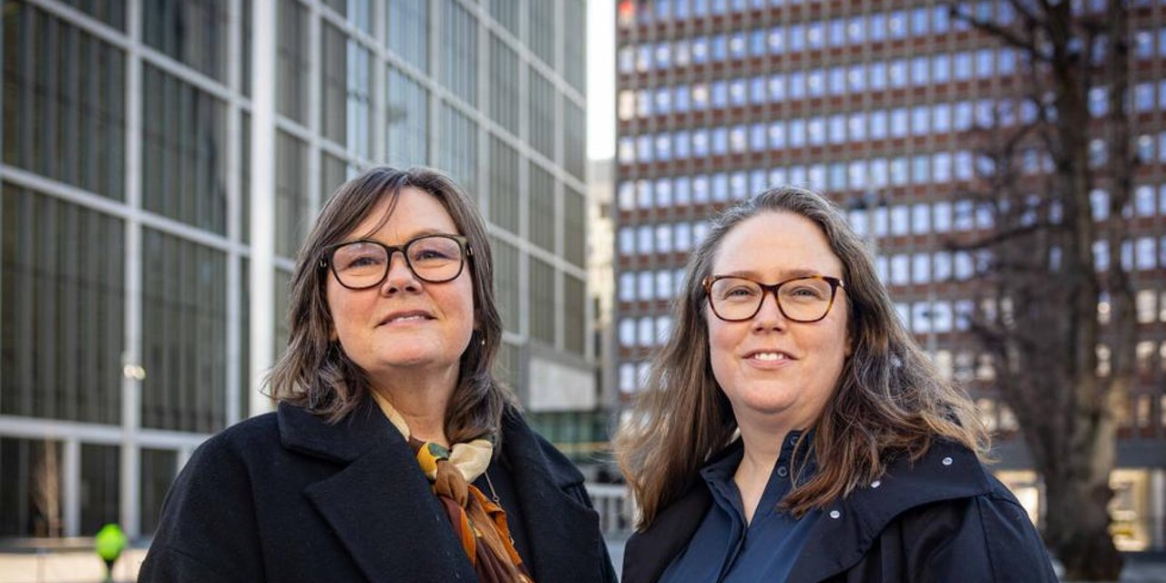 To kvinner med briller står utendørs mellom høye kontorbygg.