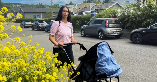 En kvinne triller en barnevogn langs en gate med gule blomster i forgrunnen.