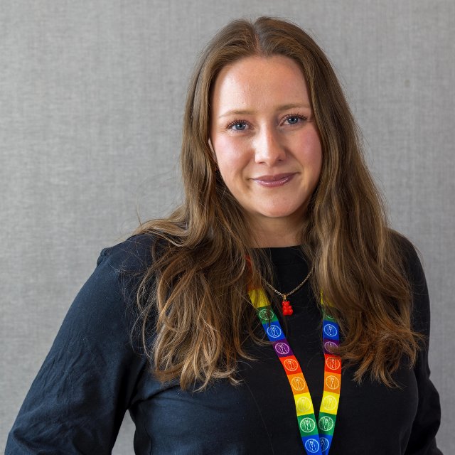 Kvinne ser smilende inn i kamera. Rundt halsen har hun et nøkkelbånd i pride-farger.
