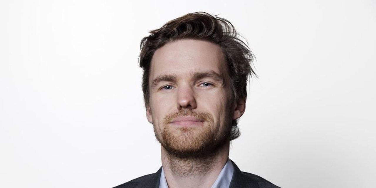 Mann ser inn i kamera, så vidt smilende, hvit bakgrunn.