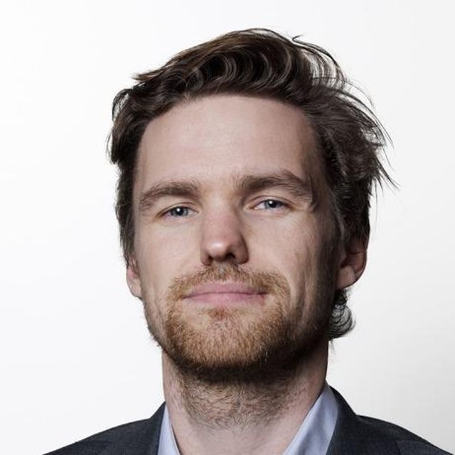 Mann ser inn i kamera, så vidt smilende, hvit bakgrunn.